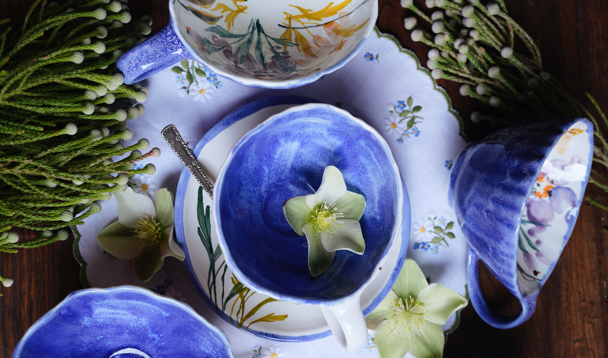 Blue ceramic teacup with floral design on a matching saucer, surrounded by greenery.